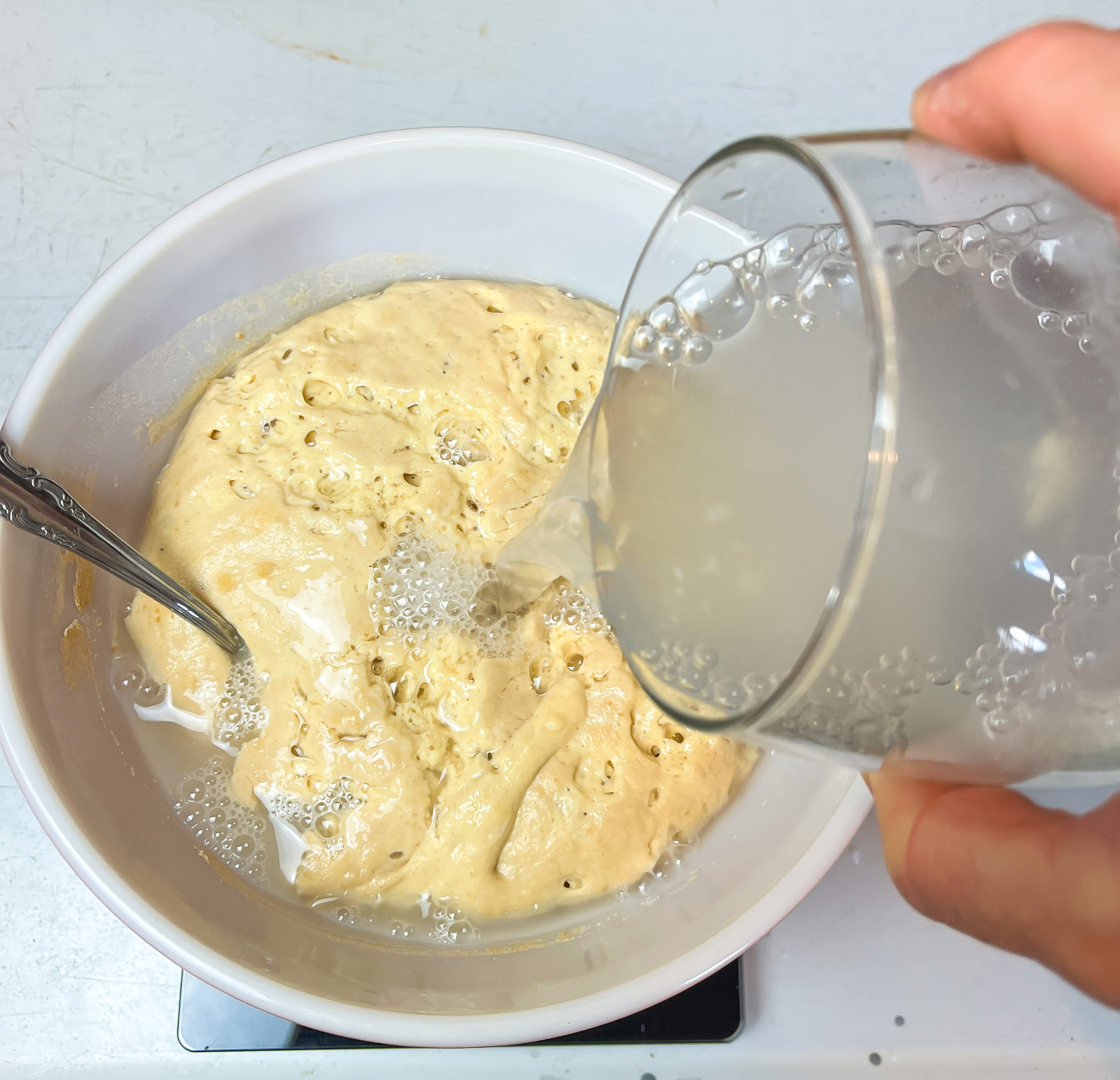 sourdough starter in a white bowl with a glass of water being poured into it