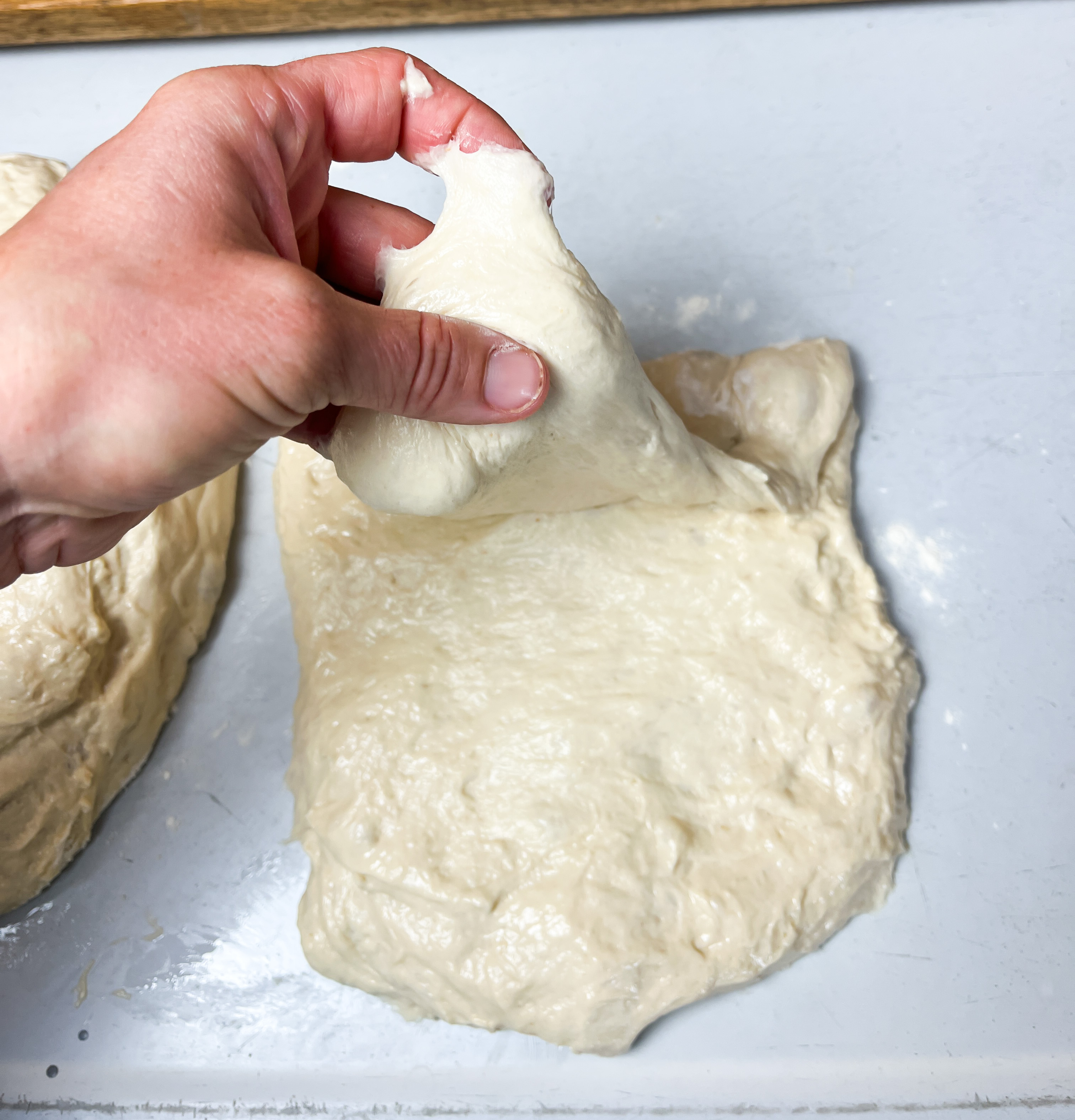 two divided piles of dough on a white countertop being folded over with a hand