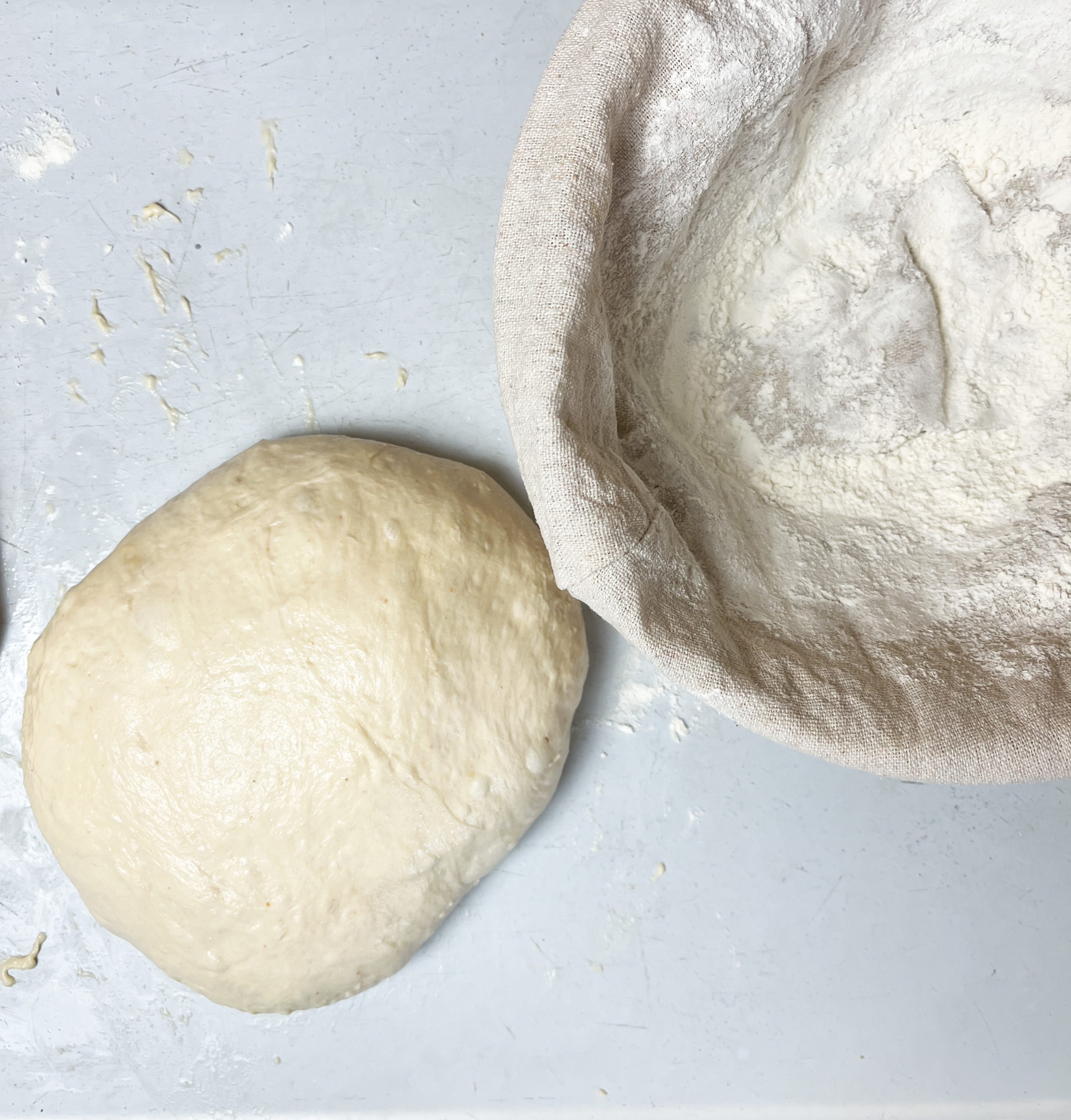 white ball of dough sitting on a white countertop with a cloth basket